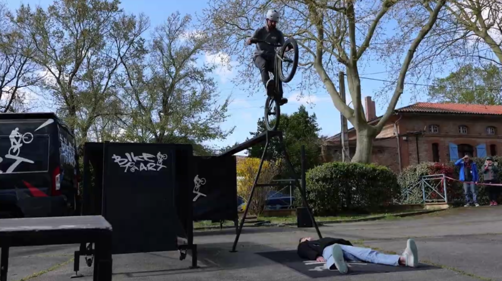 Saut de VTT trial au-dessus d'une personne allongée au sol lors du show Bike Art à Noueilles