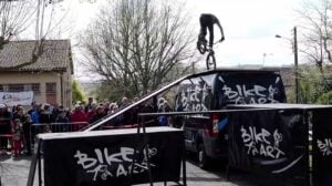 Rider Bike Art en équilibre trial sur le toit du camion, banderole SLA Qu'es Aquò et public de la Cour'SLA Pied 2026