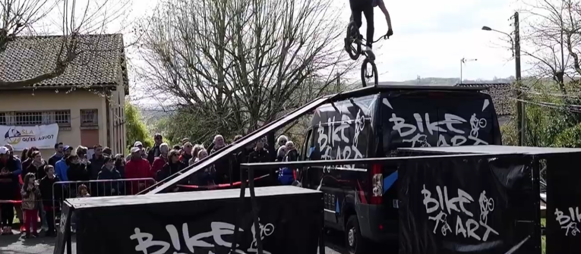 Rider Bike Art en équilibre trial sur le toit du camion, banderole SLA Qu'es Aquò et public de la Cour'SLA Pied 2026
