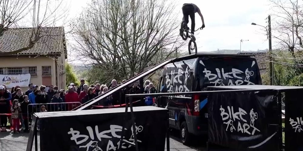 Rider Bike Art en équilibre trial sur le toit du camion, banderole SLA Qu'es Aquò et public de la Cour'SLA Pied 2026